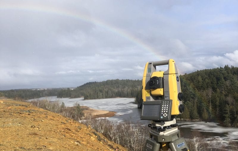 surveying equipment on a hill overlooking a river with a rainbow in the background