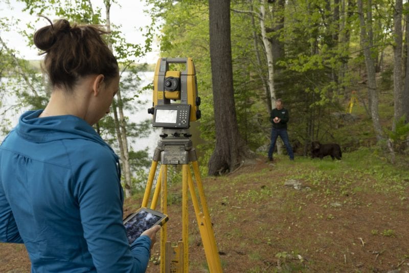tara hartson and steve salsbury using surveying equipment with their dog